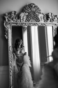 Black and white boudoir photo with Black Lace Boudoir client posing in a mirror.