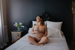 best maternity photographer near me in Virginia featuring client sitting on bed with hands on top of stomach.