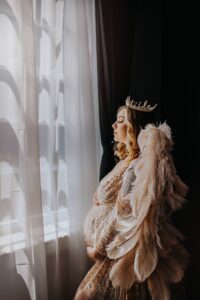 maternity boudoir photoshoot with Black Lace Boudoir featuring luxury Fredericksburg boudoir studio and client wearing gold crown posing next to a window.