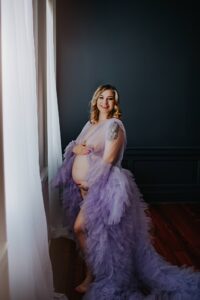maternity boudoir with Black Lace Boudoir, Maryland and Virginia featuring client in purple sheer rob posing next to a window.