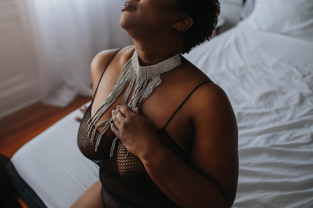 Boudoir photoshoot featuring black woman posing with silver necklace. 