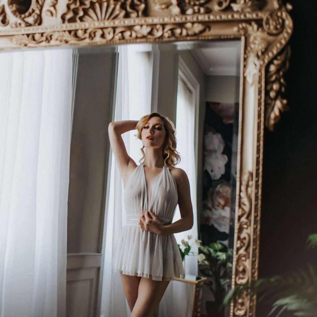 Boudoir process includes access to luxury studio. Model poses in front of gold mirror showing off the studio. 