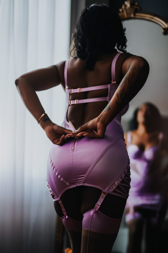 Ms. A stands in front of a full size mirror and zips up her lilac purple Lingerie that she brought from home and she can put it back on to remember her session!