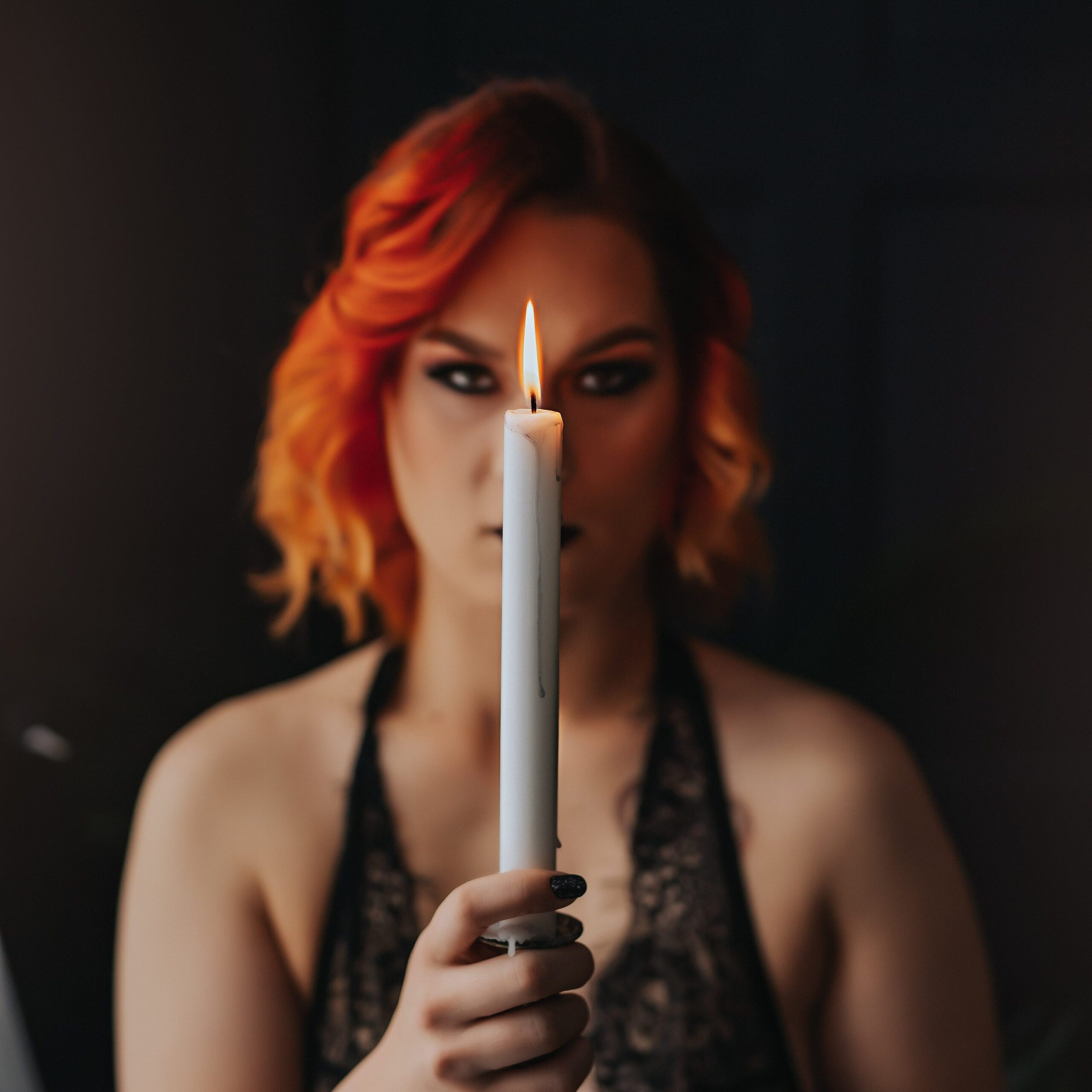 Ms. K (out of focus) holds a candle in a dark and moody photo.