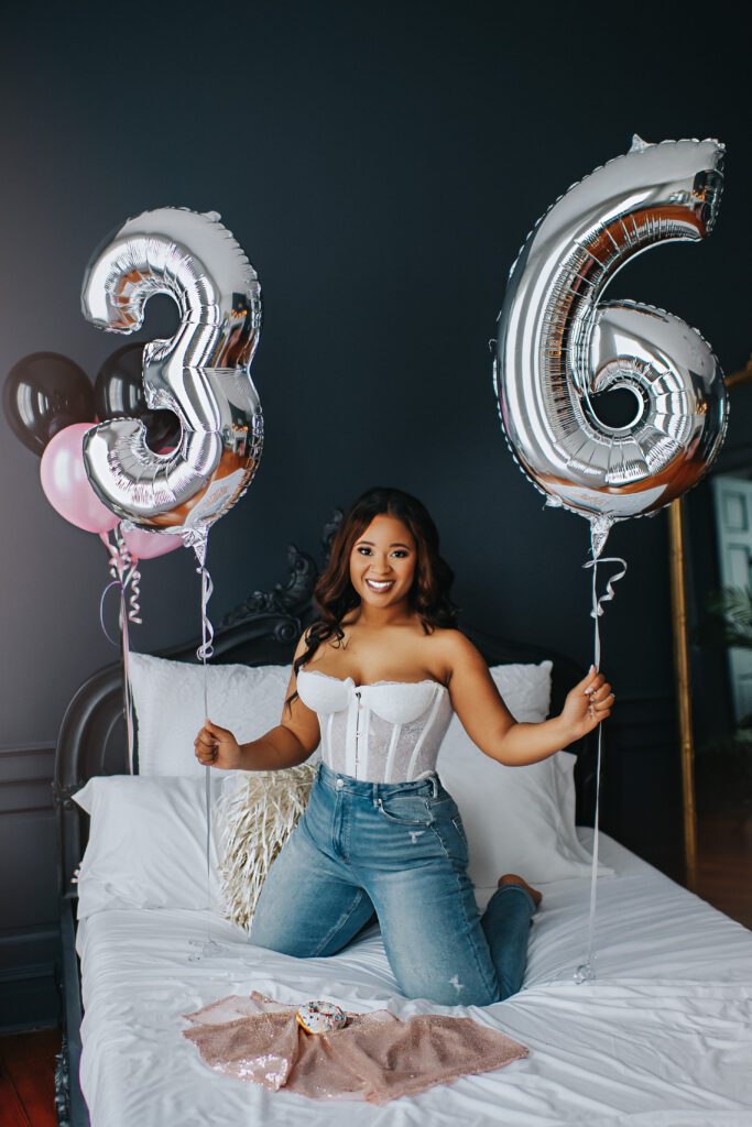 Ms. B celebrates her birthday with a birthday boudoir session. She is holding balloon numbers with her age and has a rainbow sprinkle doughnut. 
