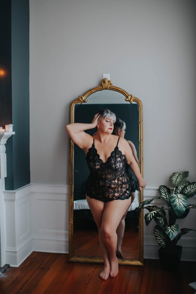 Ms K stands in front of a gold-framed mirror during her Last Minute Date Boudoir Session